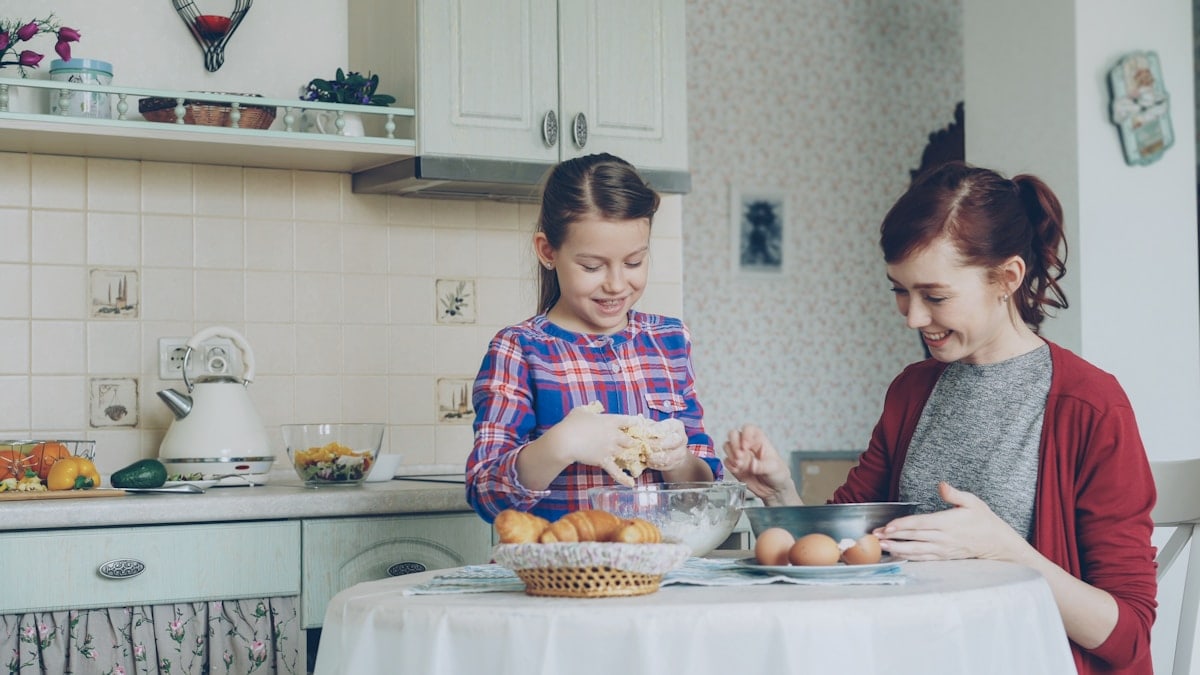 Little cute girl helping her mother in the kitchen stirring dough for cookies into bowl. Family, food, home and people concept
